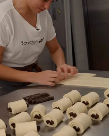 Una panadera enrolla napolitanas de chocolate una a una sobre la mesa de trabajo