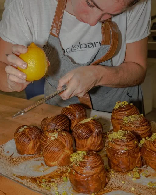 Un panadero ralla limón sobre una bandeja de cruffins de pistacho