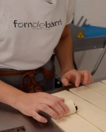 Panadero de Forn de Barri con la camiseta del obrador, laminando masa sobre la mesa